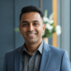 Portrait of a smiling South Asian man in smart casual attire, exuding confidence and satisfaction.
